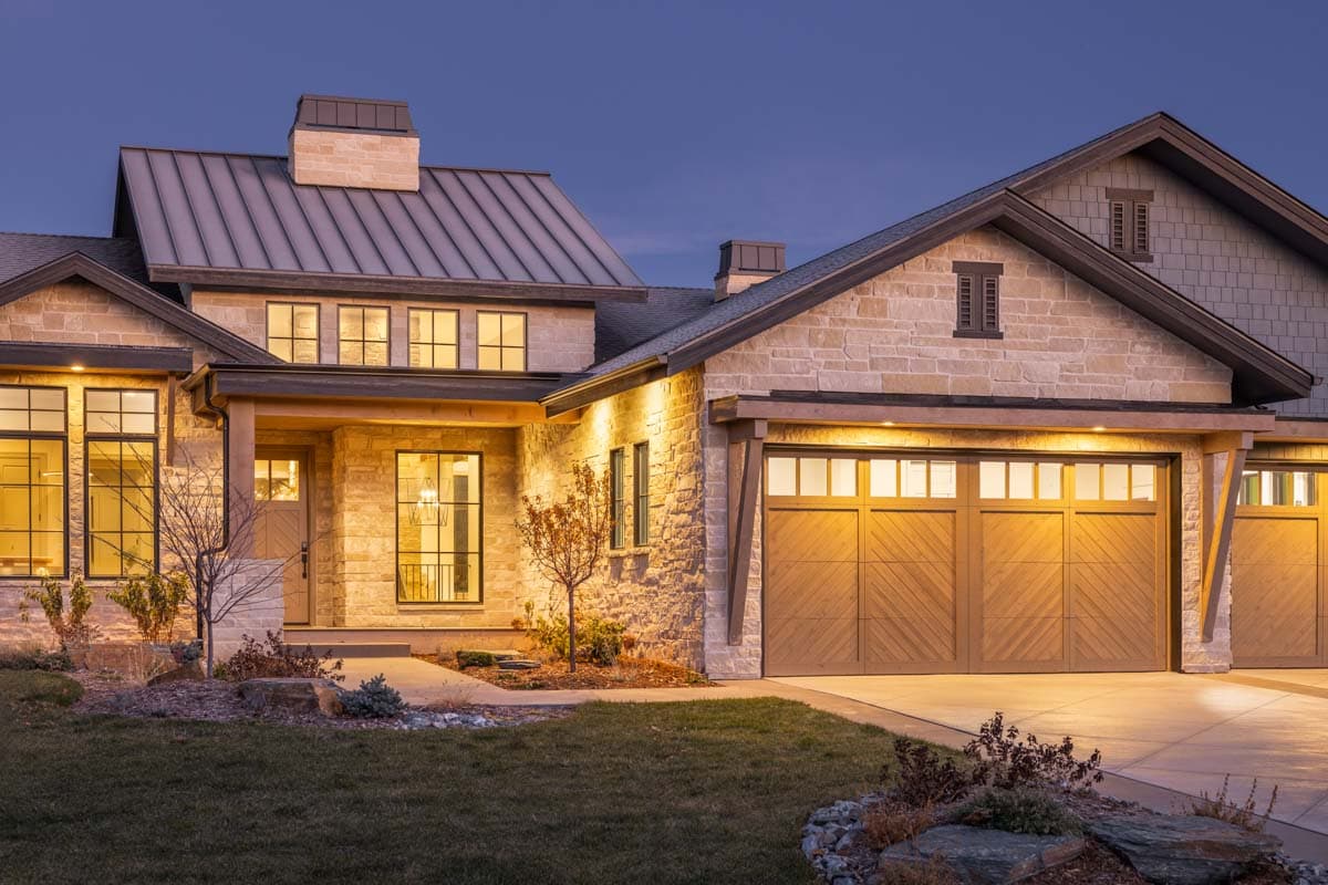 House plan exterior: Two-story Modern Farmhouse with stone and shingle siding, metal roof, prominent gable, and wood garage doors.