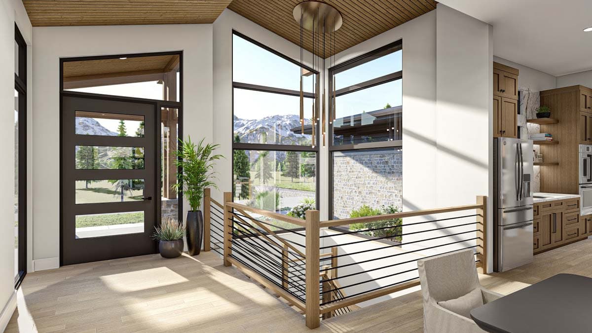 A modern home interior with a view of snow-capped mountains. A staircase with a wooden railing leads up. Large windows and a front door are visible.