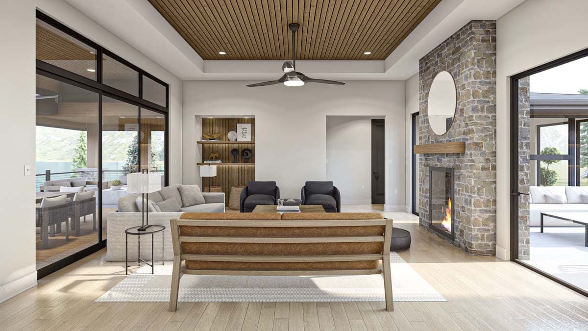 Modern living room with a stone fireplace, wooden ceiling, and large glass doors leading to an outdoor seating area and open views.