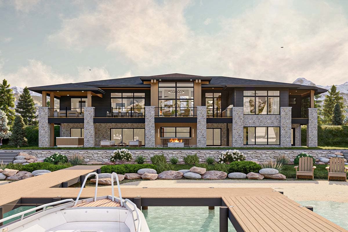 A modern waterfront home with large windows and a fireplace, featuring a wooden dock, boat, and mountain backdrop.