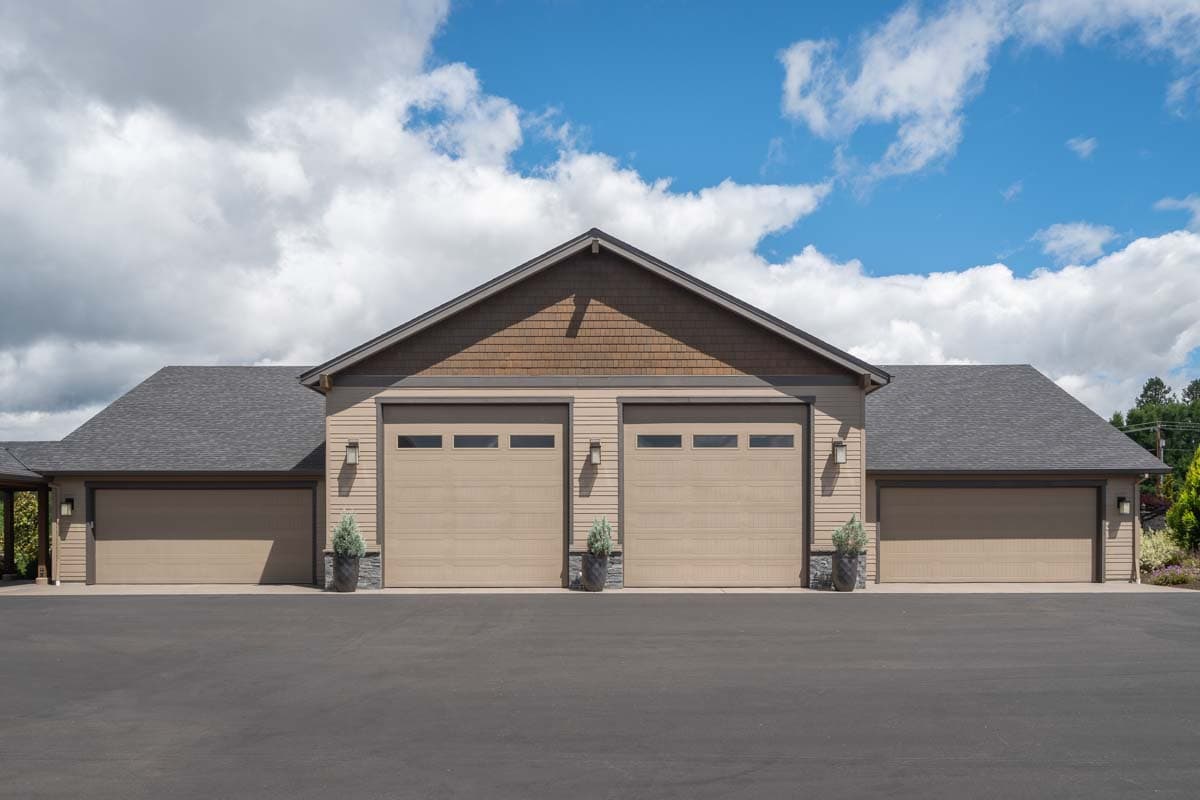 House plan exterior with multiple-bay garage, gabled roof, and cedar shake detailing above the garage doors. Three garage doors and asphalt driveway.
