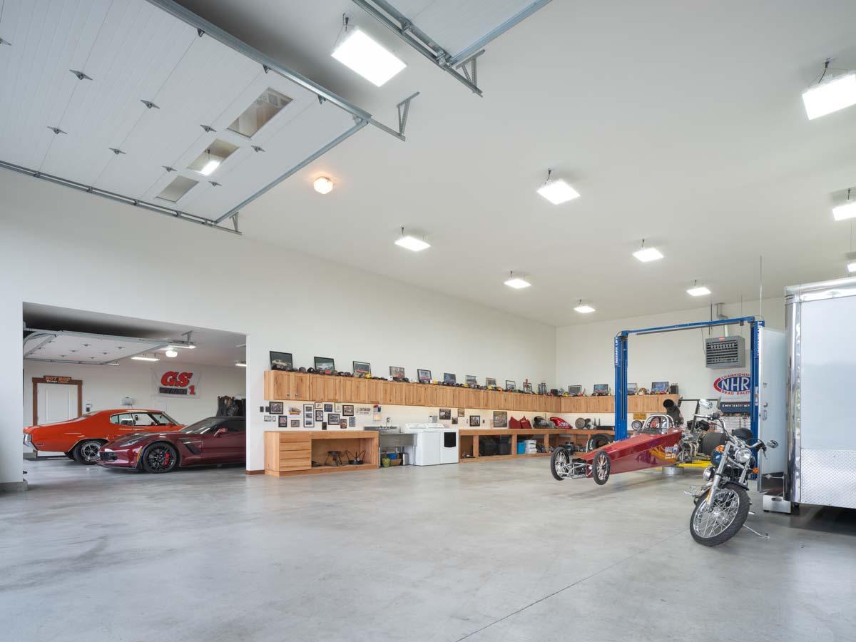 Spacious garage interior with cars, dragster on lift, motorcycle, and built-in cabinetry.
