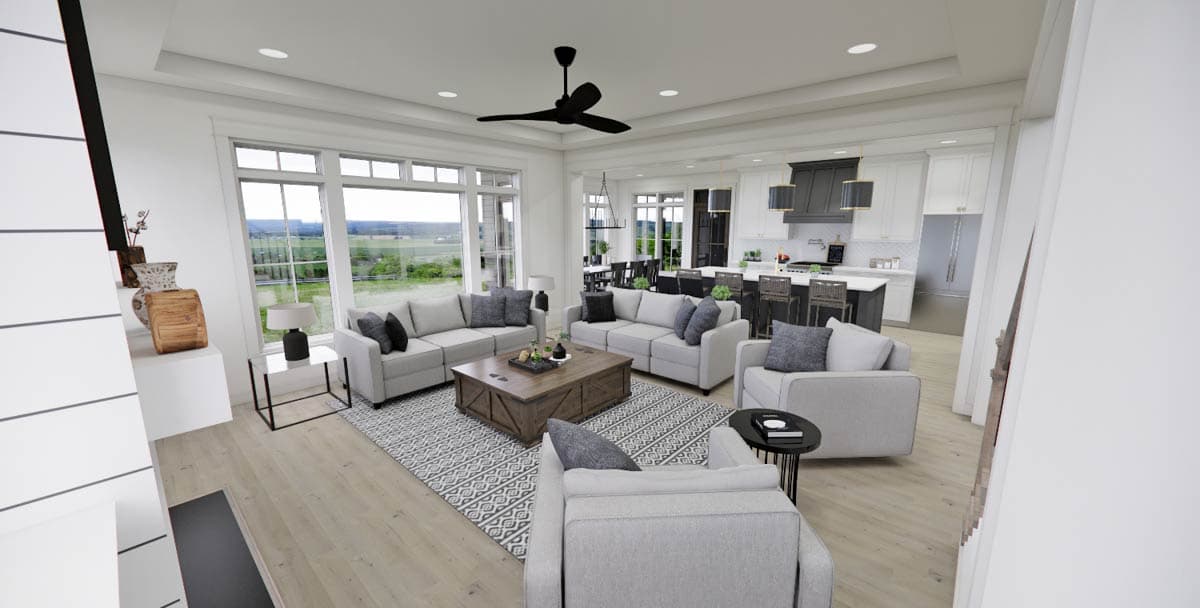 A modern, open-concept living room with light gray couches, a wooden coffee table, and large windows overlooking a green landscape.