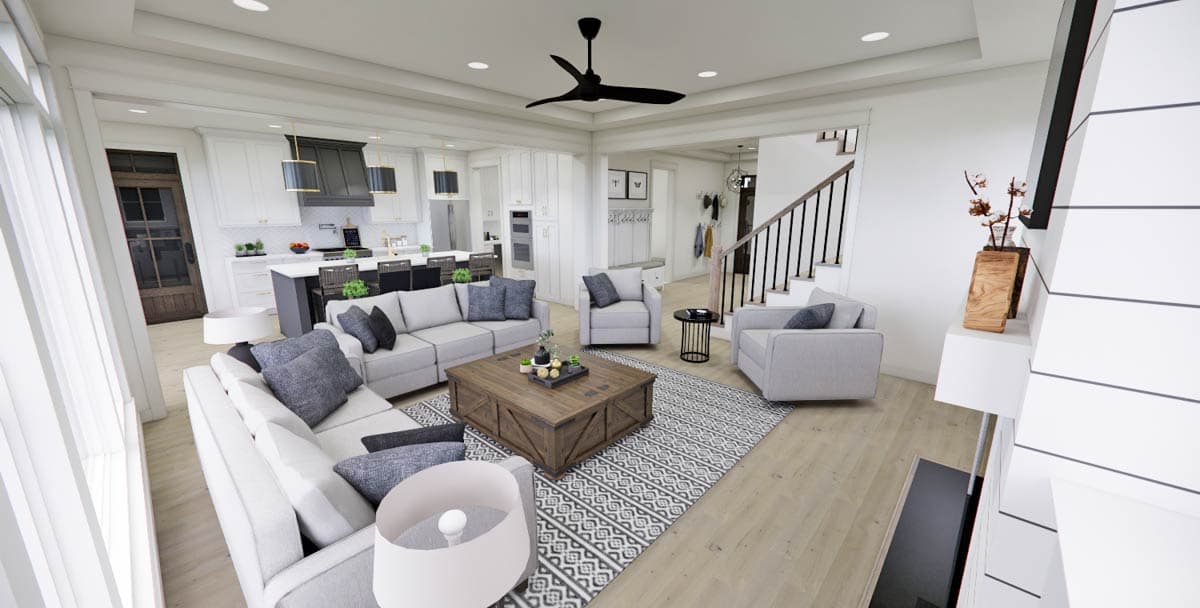 Spacious, modern living room with gray sofas, a wooden coffee table, and a patterned rug. The open concept leads to a kitchen and a staircase.