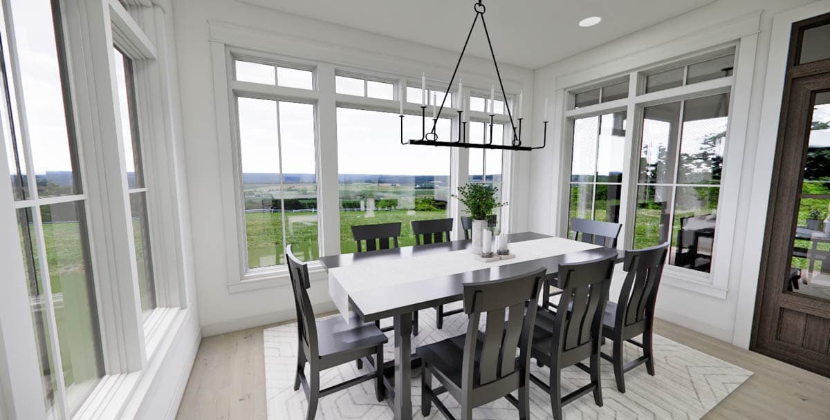Bright dining room with a large table set for a meal, surrounded by gray chairs, facing large windows overlooking a green landscape.