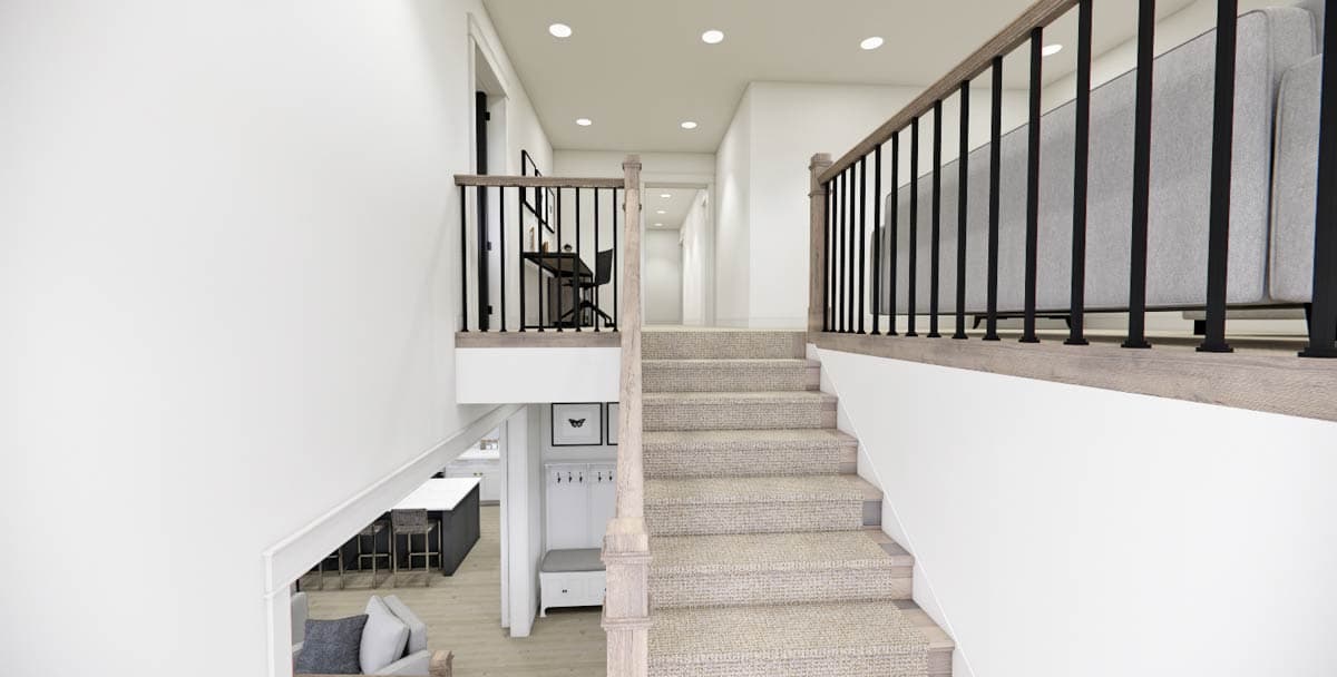 Interior view of a modern home hallway with a staircase. The stairs have carpet and a wooden handrail with black iron bars. A desk is on the landing.