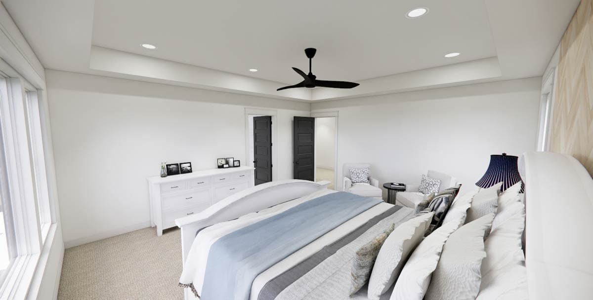 A modern bedroom with white walls, a large bed with a blue and gray comforter, and a black ceiling fan. Two chairs face the bed.