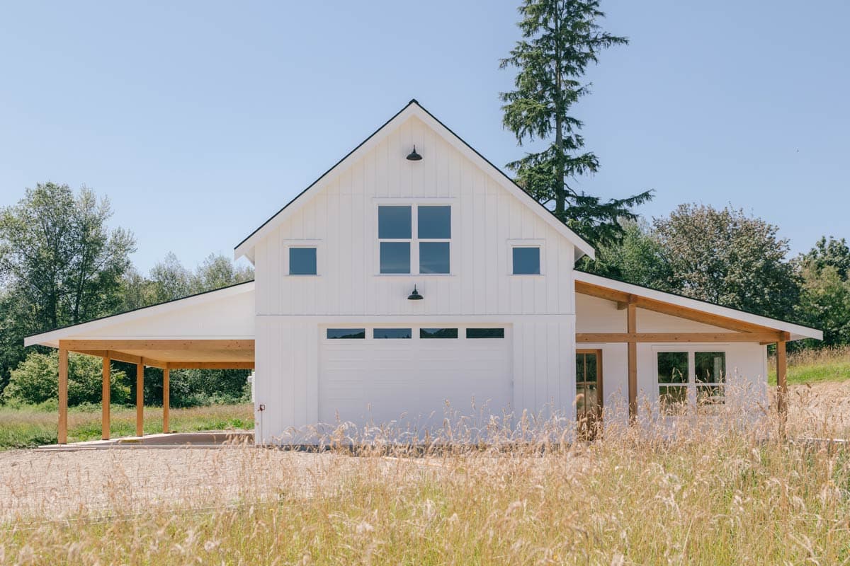 Modern farmhouse house plan exterior with white board and batten siding, a covered carport, and a prominent gable with garage door.