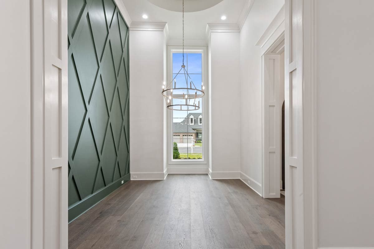 Interior hallway with geometric accent wall, tall window revealing exterior, and circular chandelier.