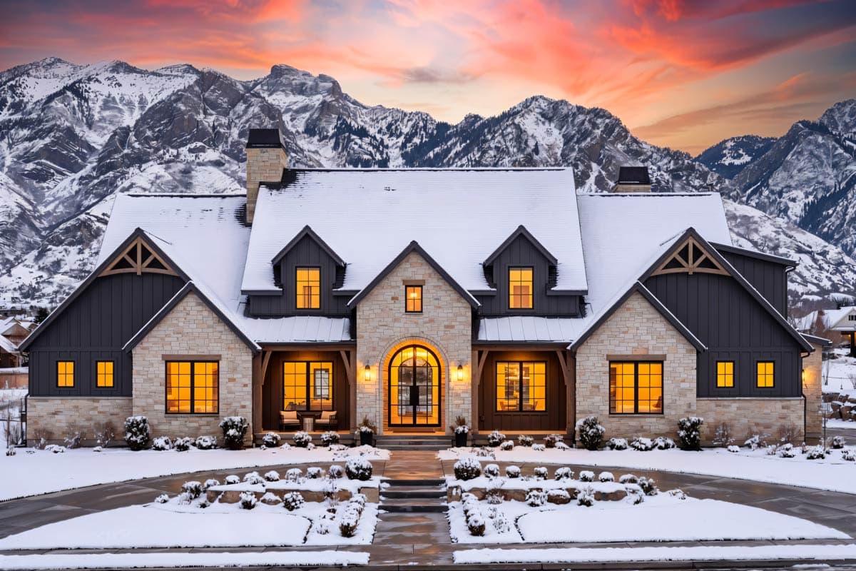 House plan exterior with stone and dark siding, pitched rooflines, dormers, and an arched entryway, set against a snowy mountain backdrop.