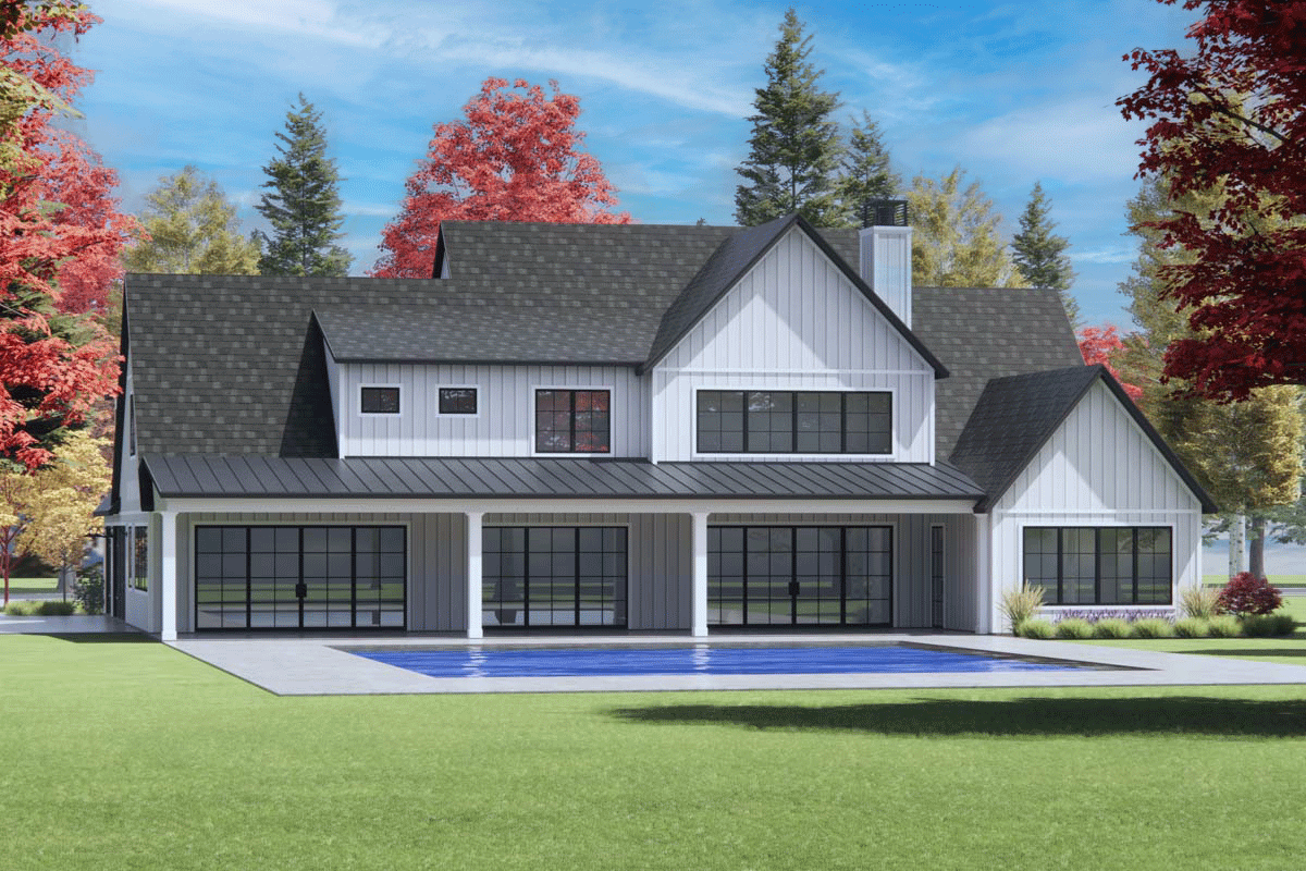 A modern farmhouse with a pool and a backdrop of vibrant fall foliage. The home features black-framed windows and a dark gray roof.