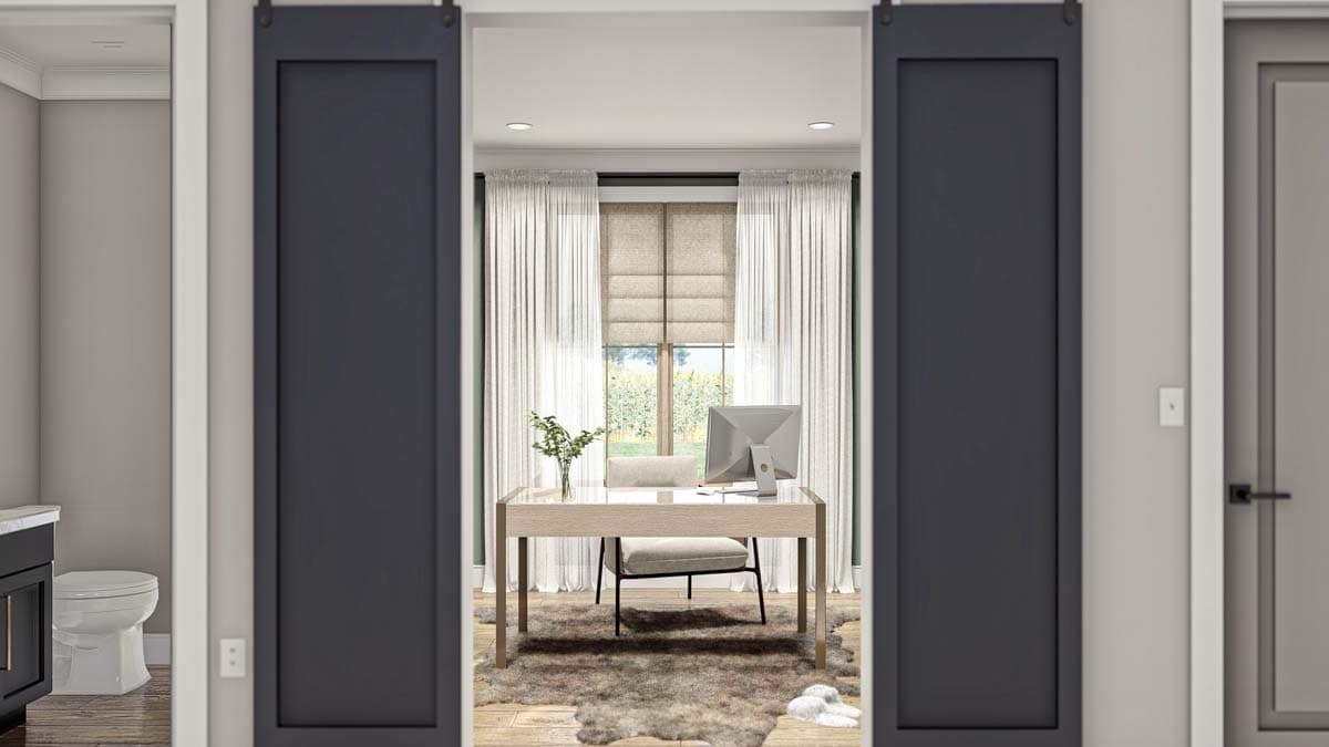 View into a home office with desk, computer, chair, and large window framed by barn doors. Toilet visible to the left.