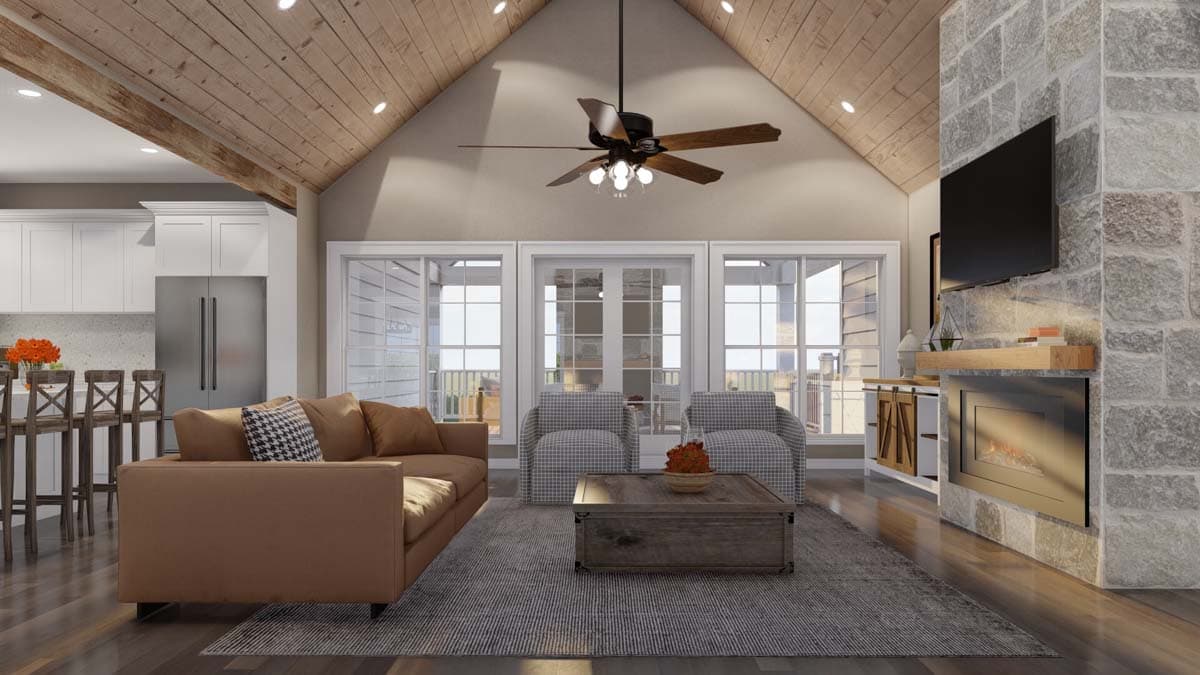 Living room with vaulted ceiling, stone fireplace, media console, and adjacent kitchen with island and stainless steel appliances.