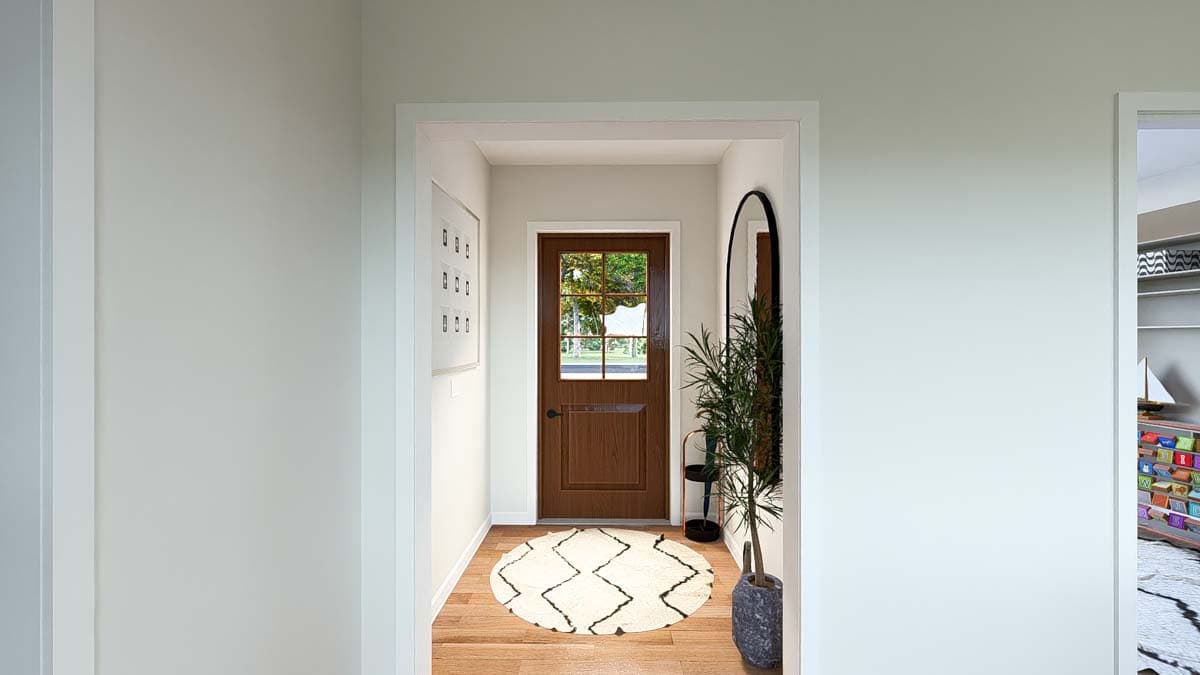 Interior view of a hallway with a wooden door, round rug, plant, and framed artwork on wall.