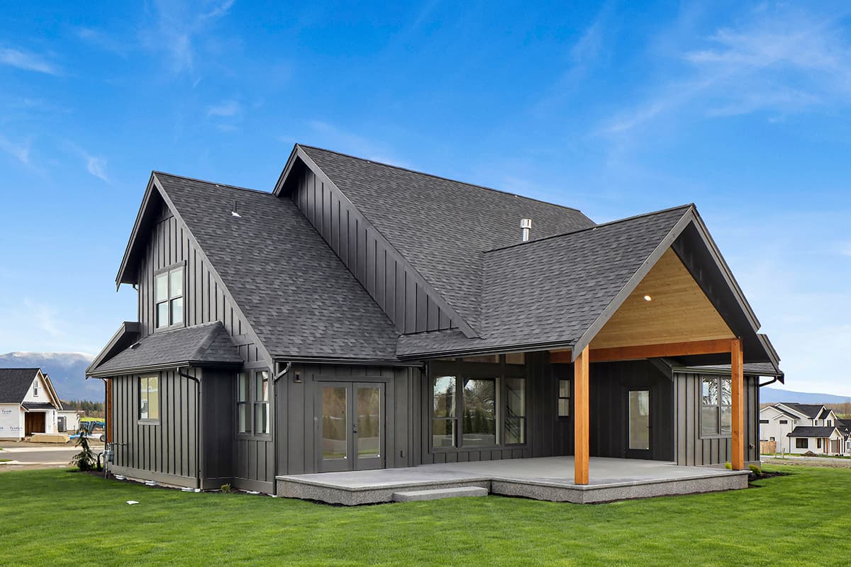 Modern Farmhouse house plan exterior with dark vertical siding, gables, dormers, and a covered patio with wood accents.