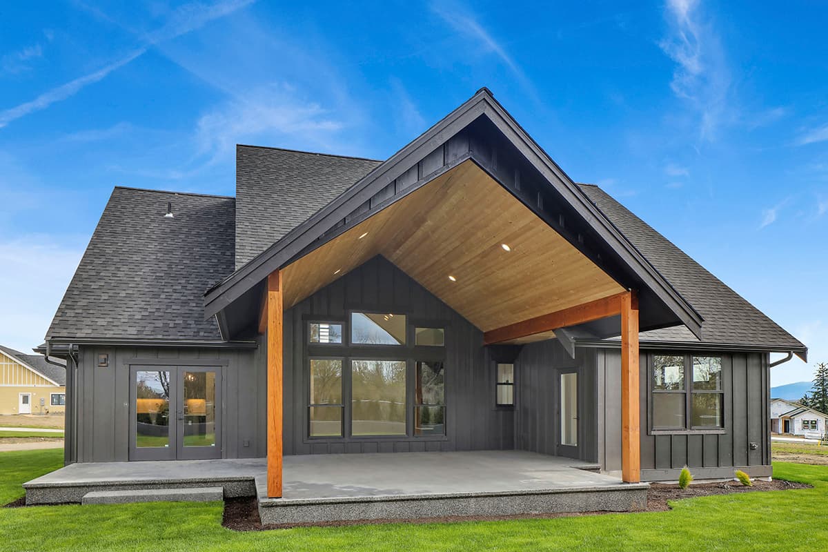Modern house plan exterior with a covered patio, large windows, gabled rooflines, and dark vertical siding.