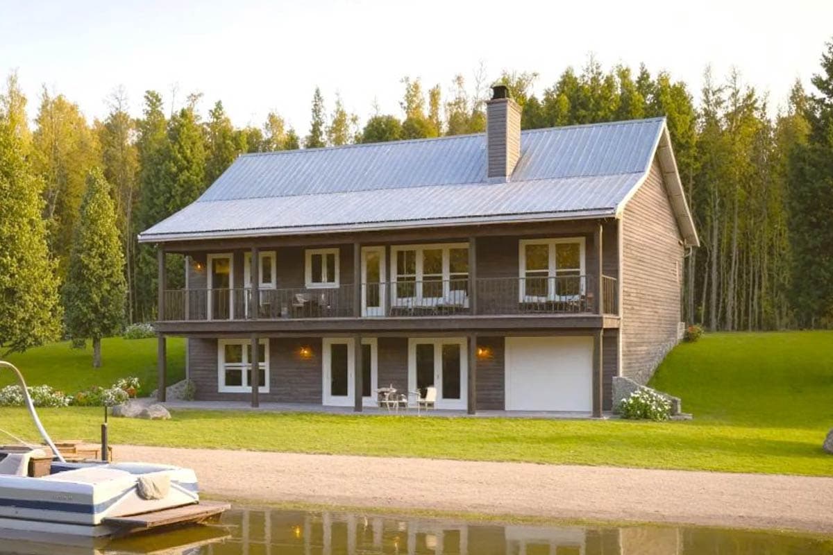 House plan exterior: Two-story modern home with a full-length upper porch, metal roof, gabled dormers, and a side-facing garage door.