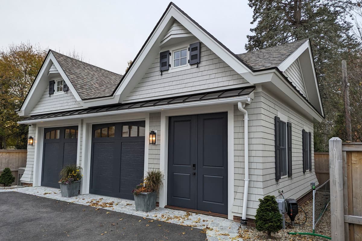House plan exterior with two garage doors, a double entry door, gable dormers, and shaker siding.