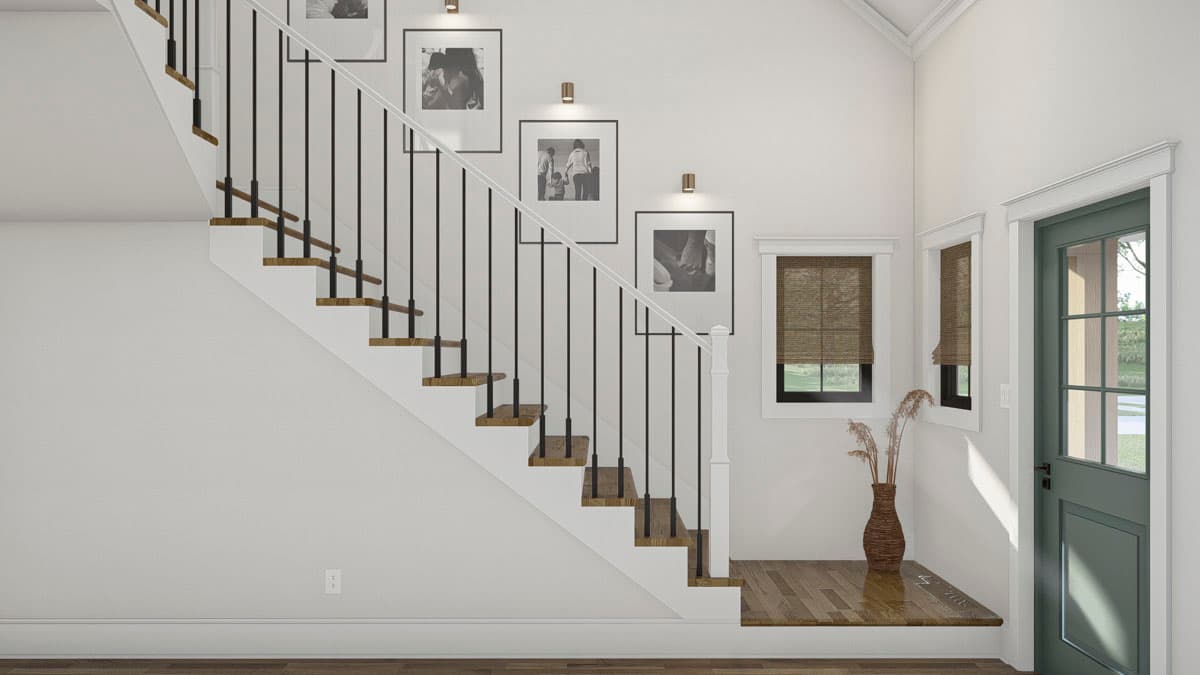 Interior view of a staircase with wood treads, white risers, and black balusters. Includes framed photos and a green paneled door.