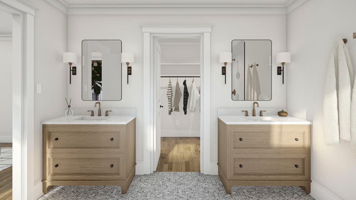 Bathroom interior with dual wood vanities with white countertops, mirrors, wall sconces, and doorway to walk-in closet.