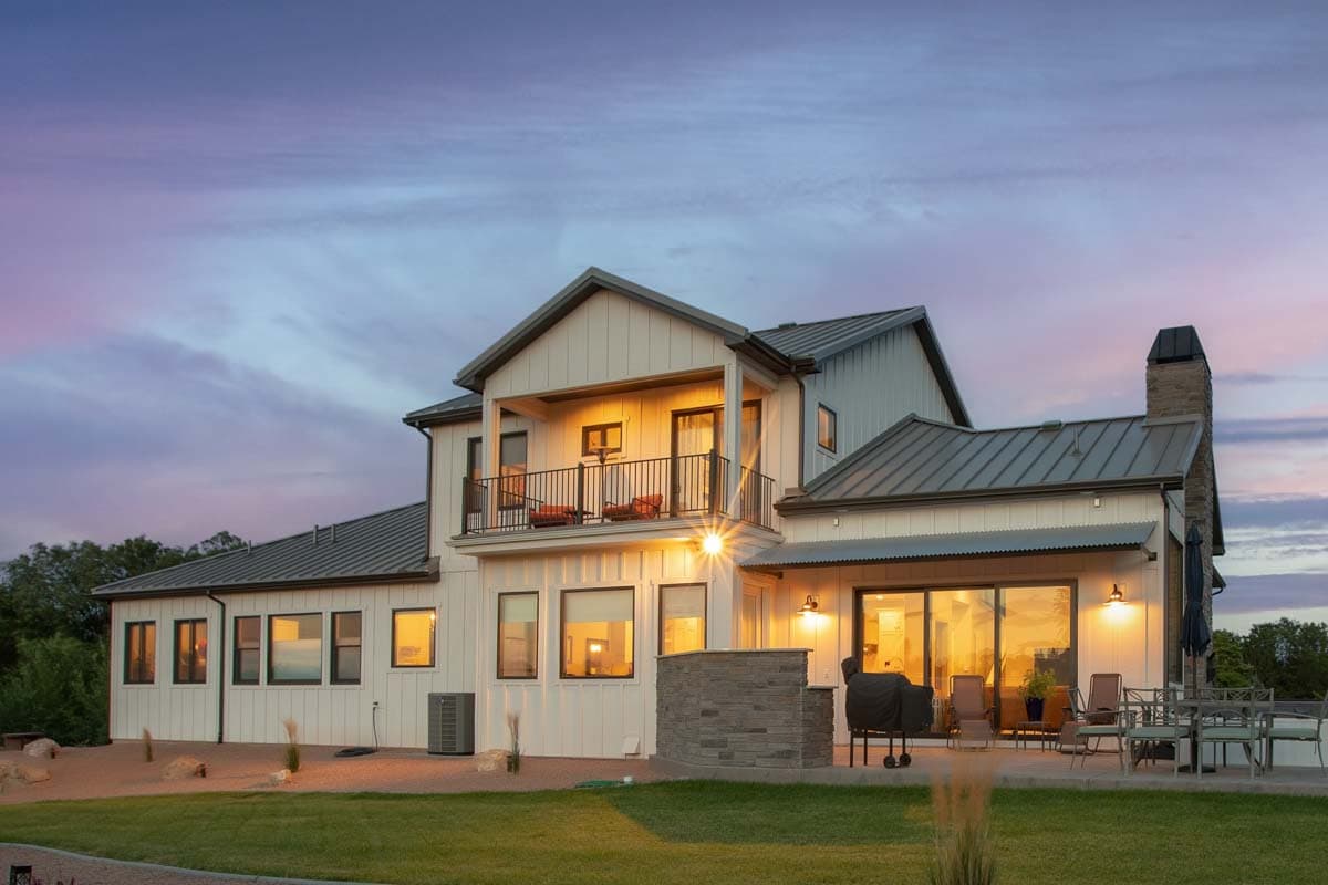 Modern Farmhouse house plan exterior with white vertical siding, metal roof, second-story balcony, and stone chimney.
