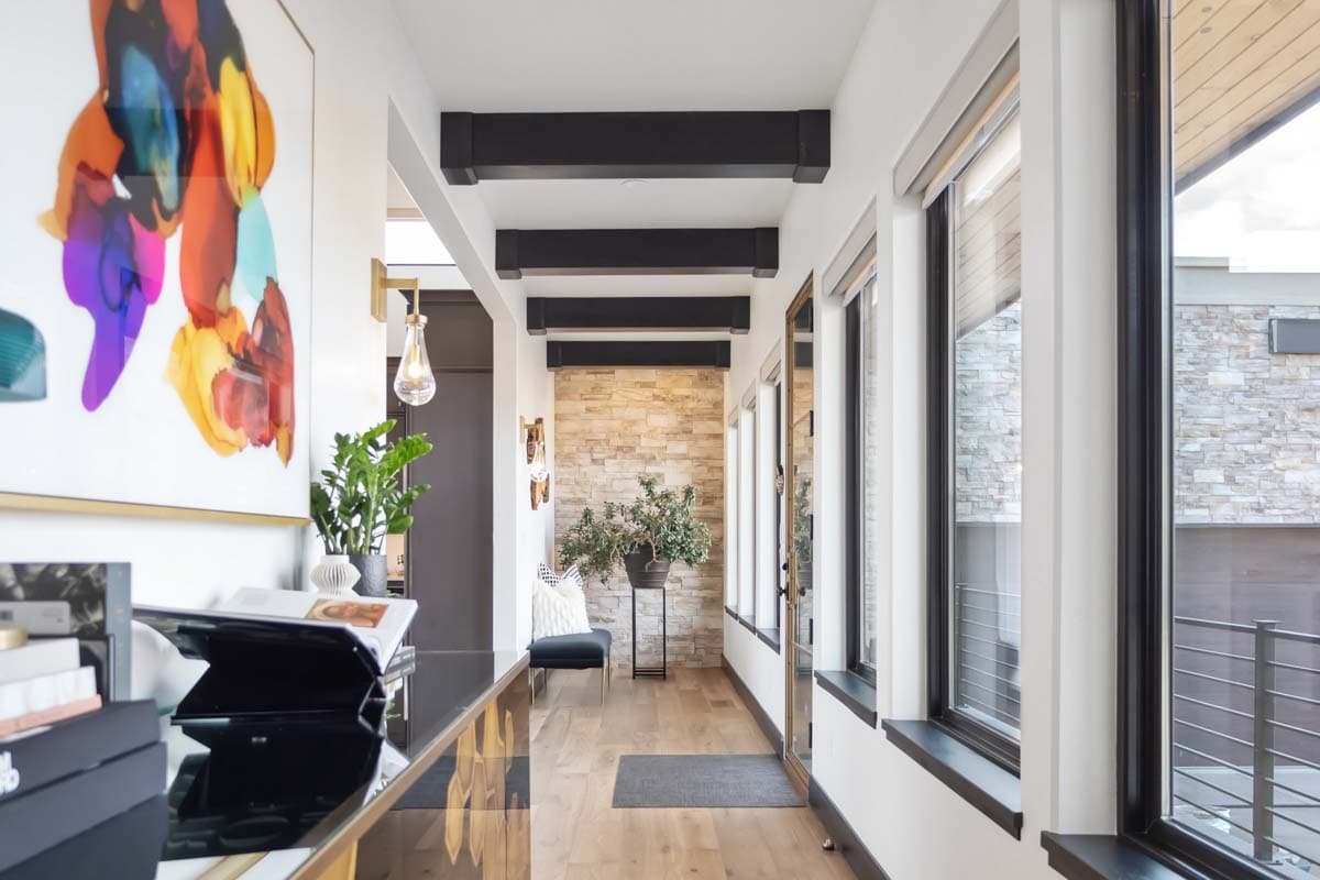 Interior view of a hallway with exposed dark beams on the ceiling, stone accent wall, and large windows.