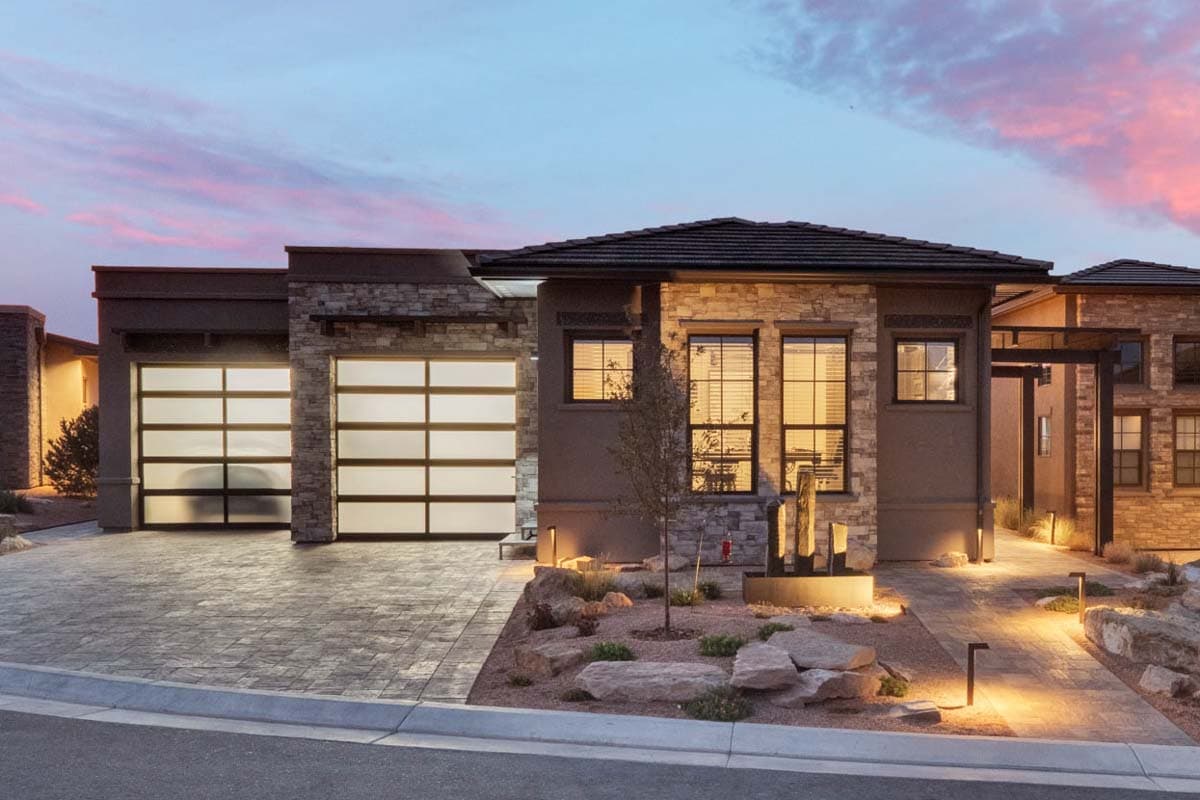 House plan exterior with a modern style, featuring two glass garage doors, stone and stucco facade, and multiple windows.