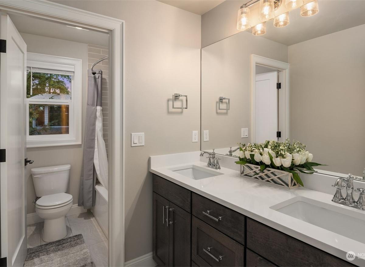 Bathroom with double vanity, white quartz countertops, dark wood cabinetry, dual sinks, and a separate toilet and tub area with a window.