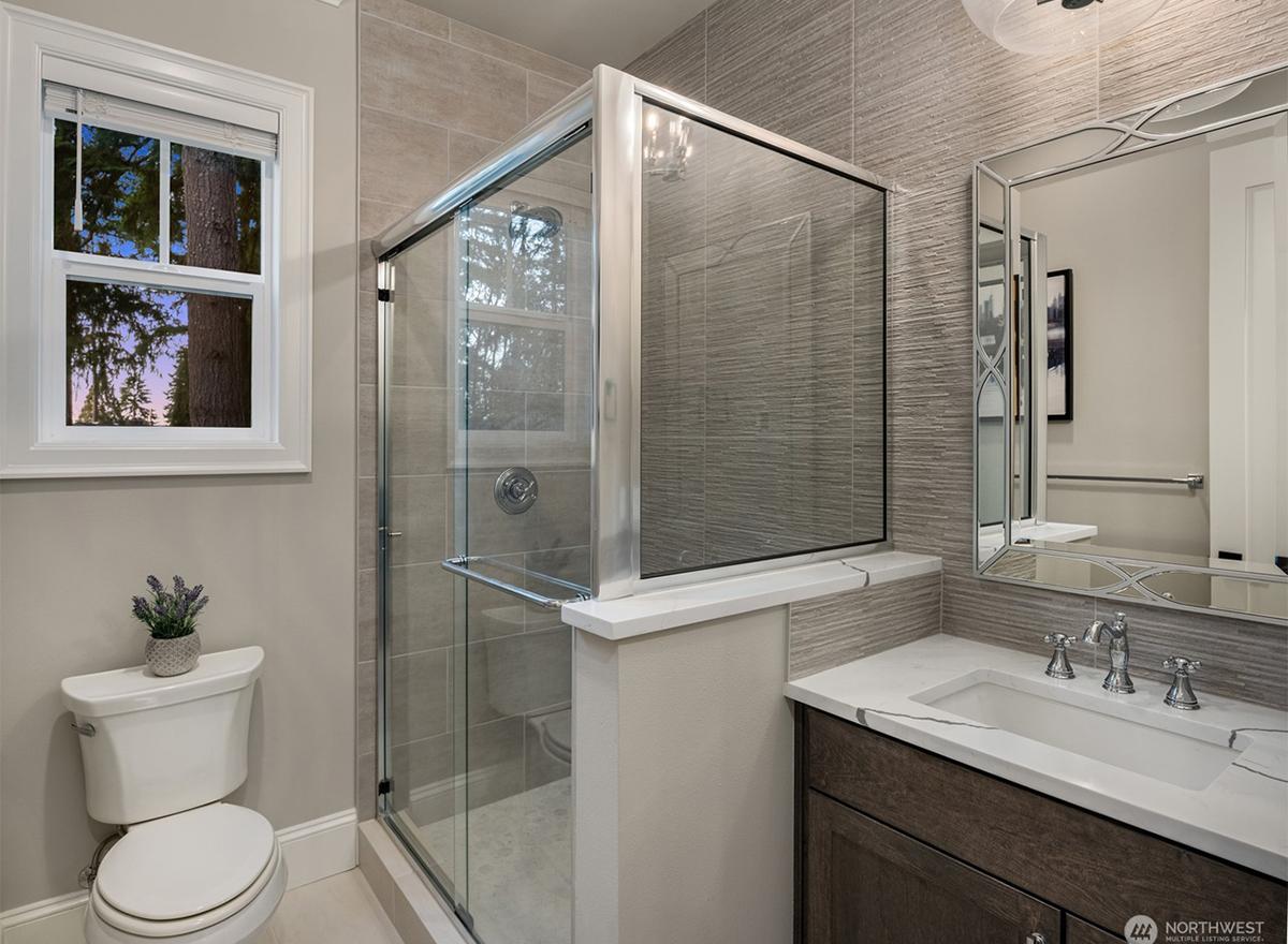 Bathroom with glass-enclosed shower, white toilet, vanity with marble countertop, and decorative mirror.