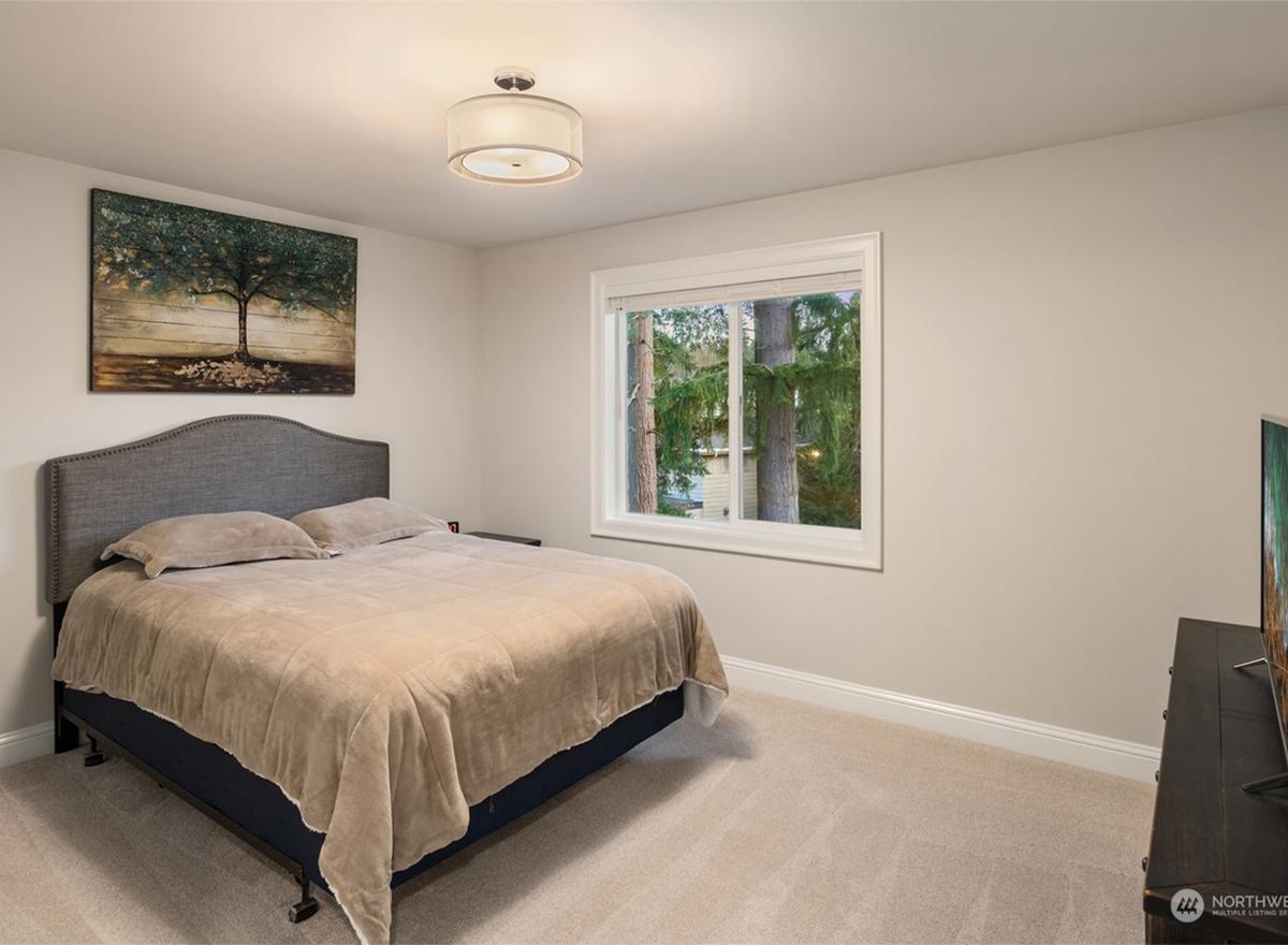 Bedroom with queen bed, upholstered headboard, artwork, large window, and ceiling light.