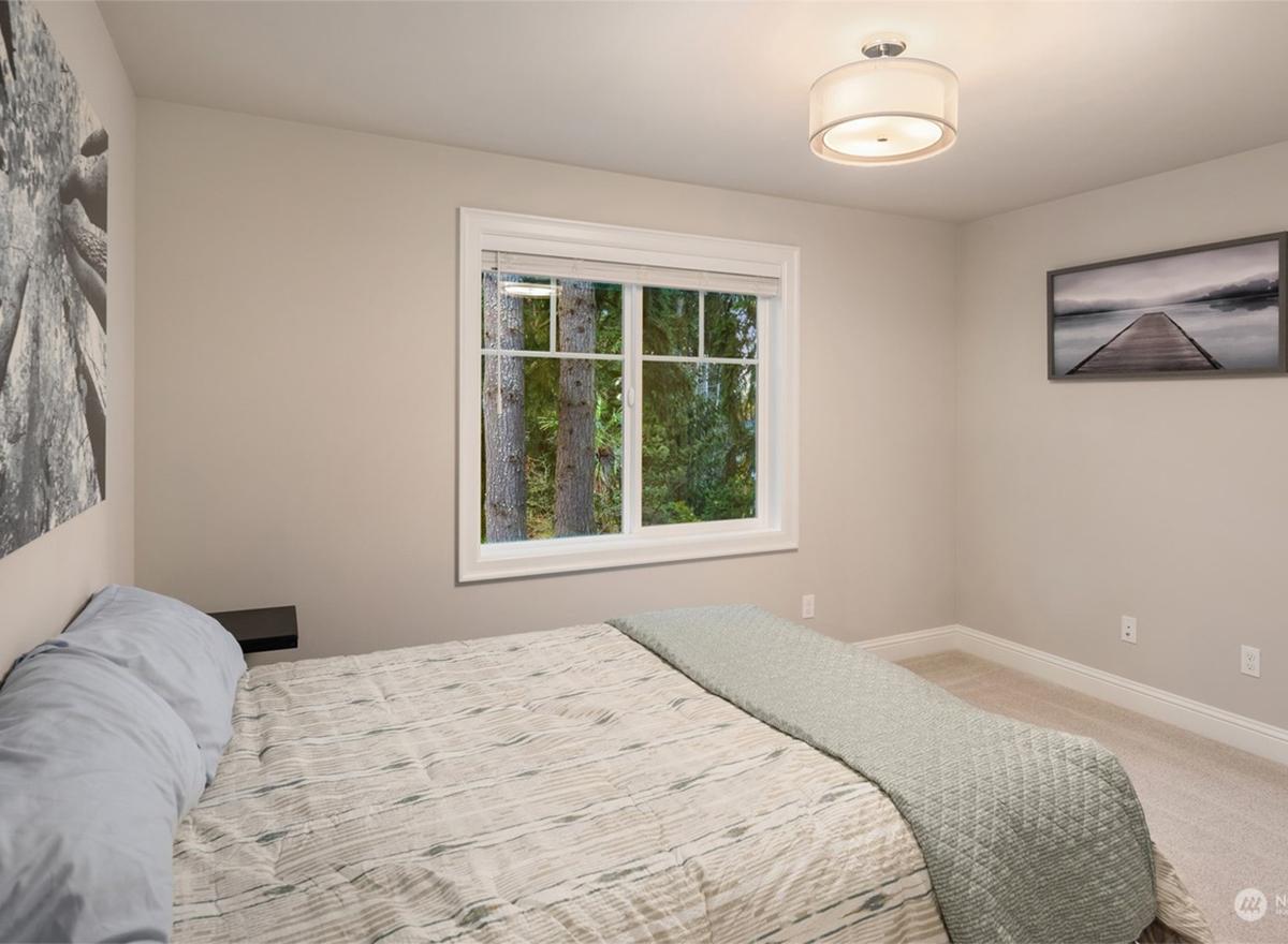 Bedroom with a double window overlooking trees, a bed with a light green throw, and two wall art pieces.