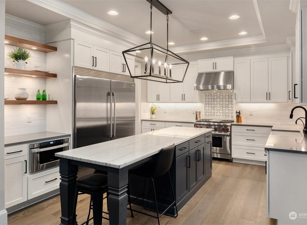 Modern kitchen with white cabinetry, stainless steel appliances, large island, and geometric pendant lighting.