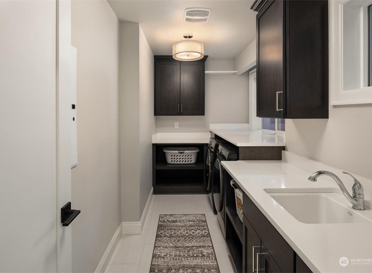 Laundry room with dark wood cabinets, white countertops, washer, dryer, sink, and basket.