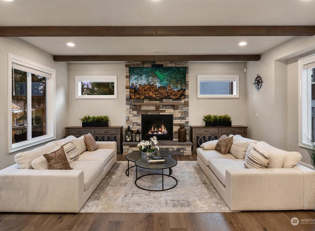 Living room with stone fireplace, mounted television, two sofas, exposed wood beams, and decorative consoles.