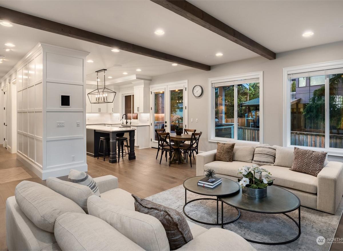 Open concept living area with kitchen island, dining table, and sofas. Exposed wood beams accent the ceiling.