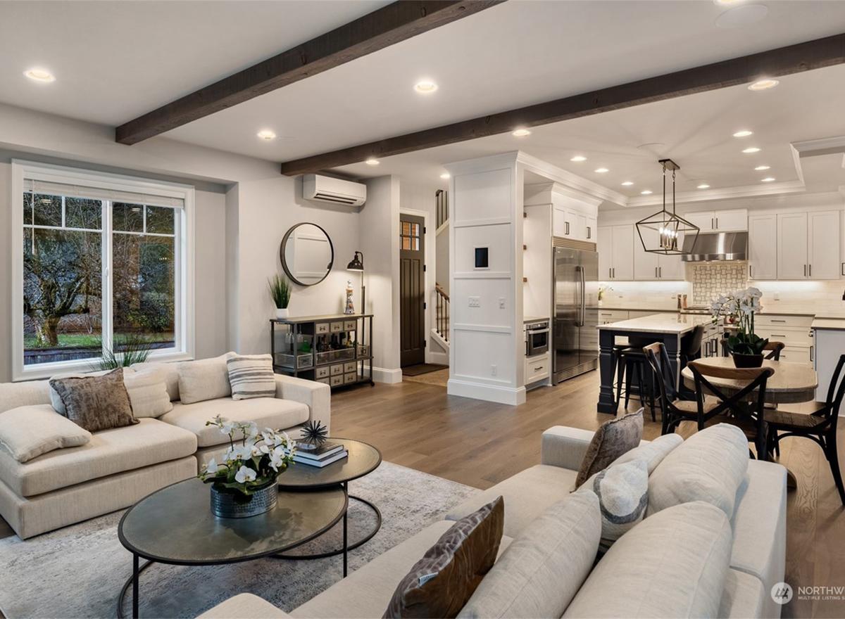 Open concept living area with sectional sofa, beamed ceiling, and view into kitchen with island and dining area.