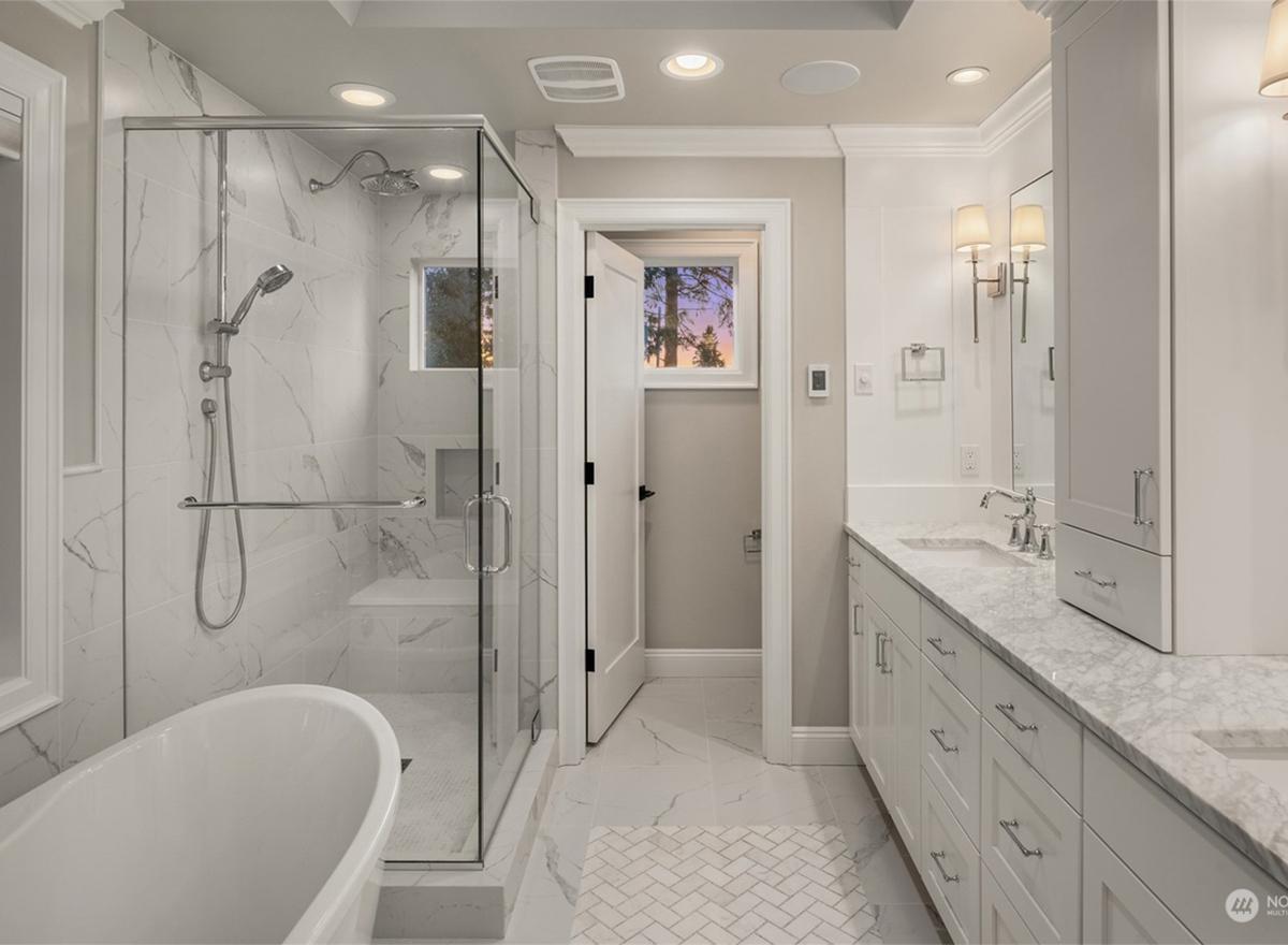 Primary bathroom with freestanding tub, glass-enclosed shower, double vanity with marble countertop, and white cabinetry.