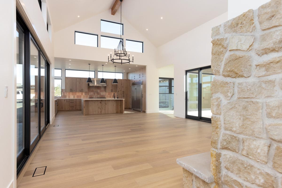 Spacious, modern kitchen with hardwood floors, a stone wall, and high ceilings. A chandelier hangs above the island, next to kitchen cabinetry.