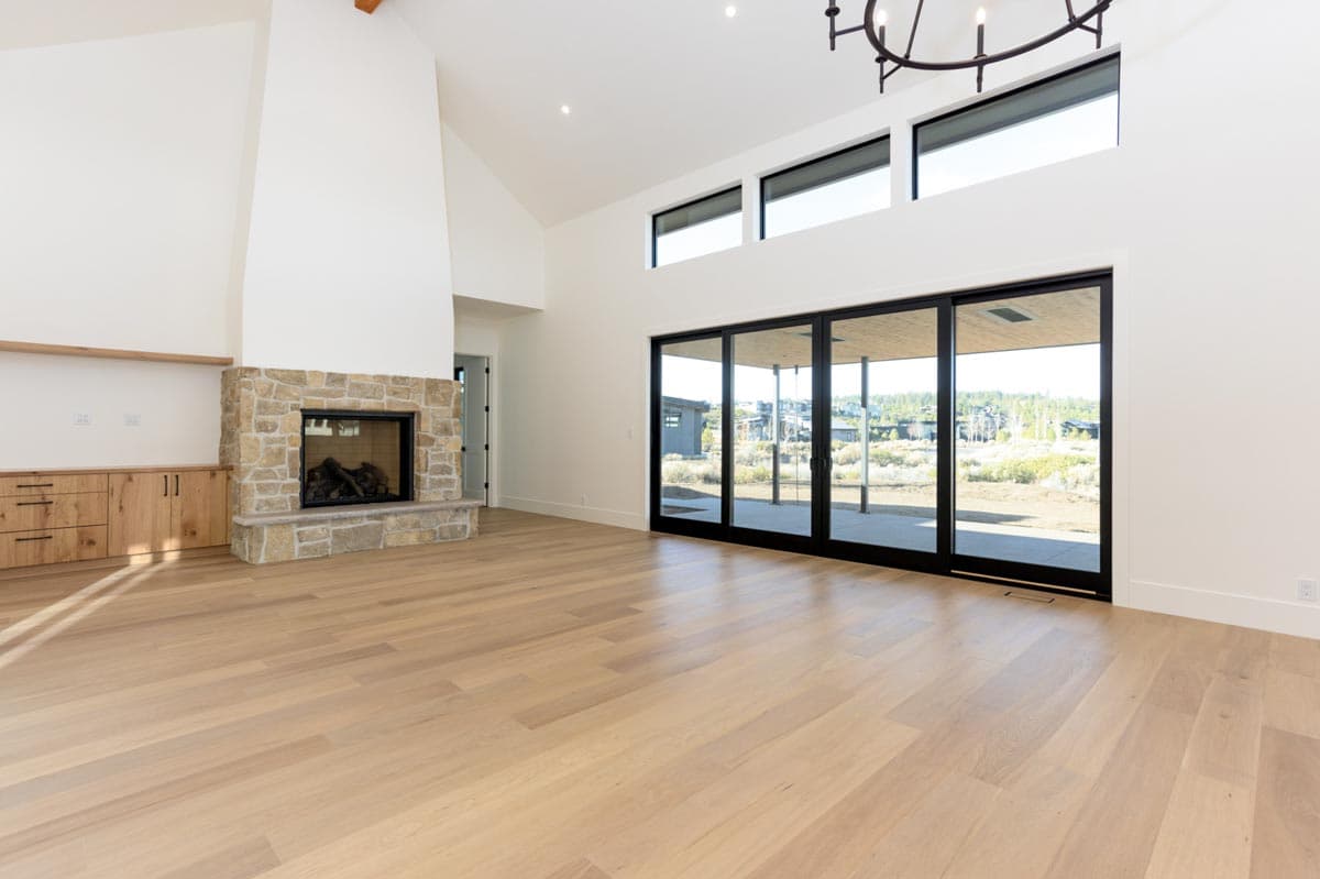 Spacious modern living room with a stone fireplace, light wood floors, and large glass sliding doors offering a view of the outside.