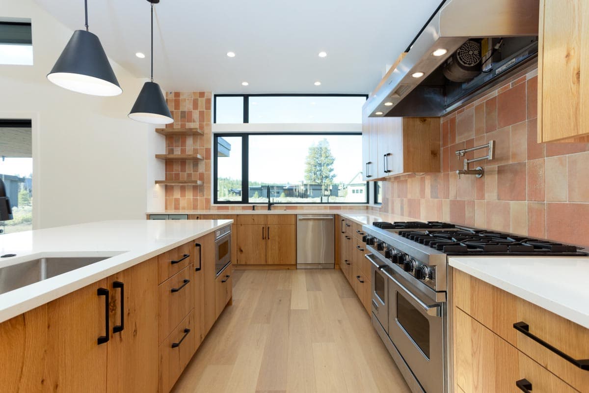 Modern kitchen with wood cabinets, white countertops, and stainless steel appliances. Large window offers a view of the outdoors.