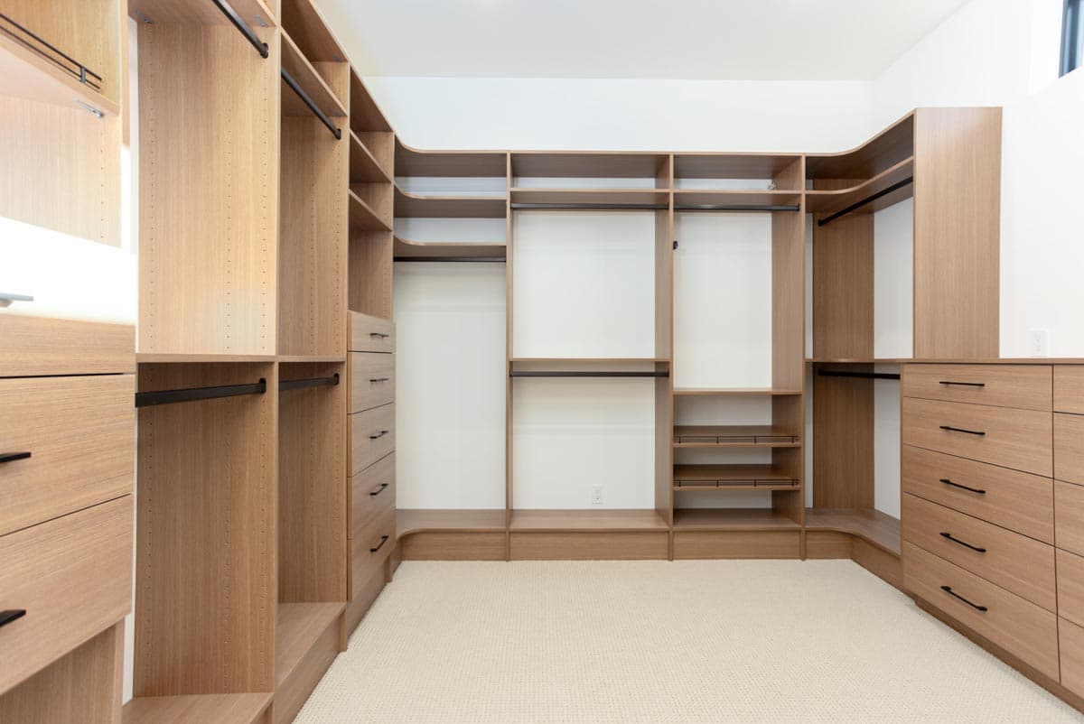 Spacious walk-in closet with custom built-in shelving, drawers, and hanging rods. The light wood provides a modern and luxurious feel.