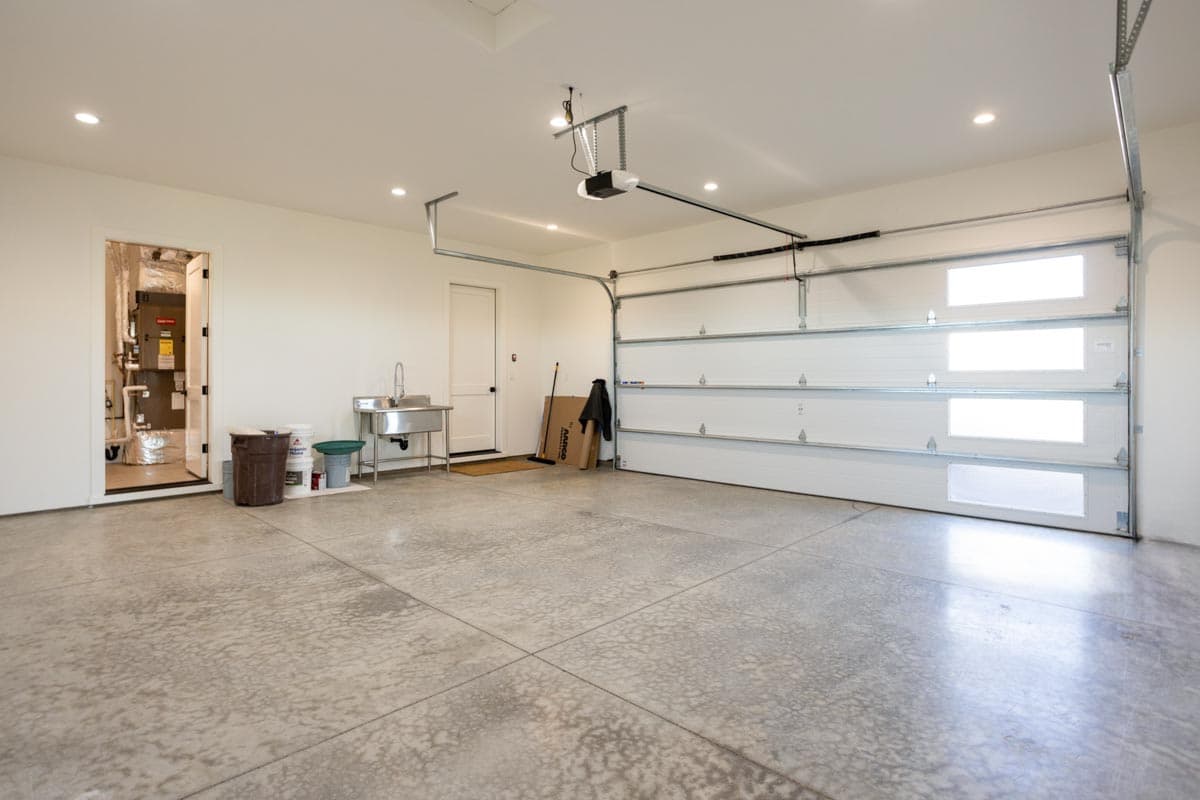An empty, freshly-cleaned garage with a concrete floor. A door leads to the house, and the garage door is partially open, revealing sunlight.