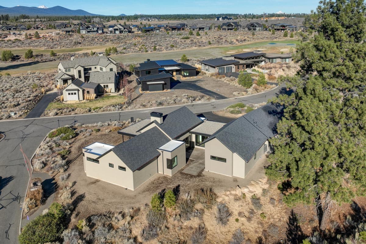 Aerial view of a modern neighborhood featuring contemporary homes with dark gray roofs nestled in a desert landscape with mountain backdrop.