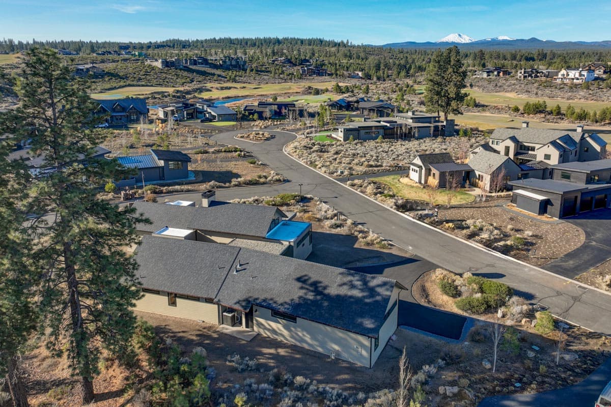 Aerial view of a modern neighborhood with luxury homes, winding roads, and a golf course. Mountains are visible in the background under a blue sky.