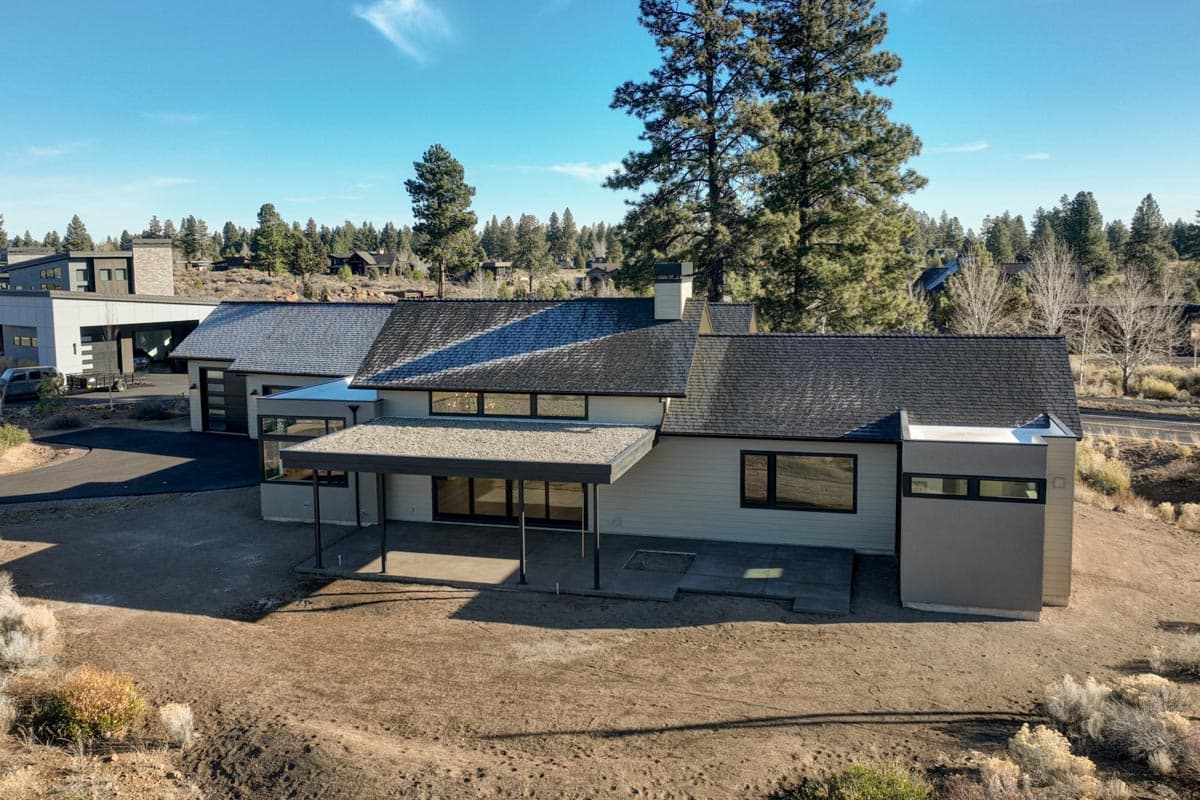 Modern single-story home with a flat roof, large windows, and a covered patio, set in a dry, grassy landscape under a clear blue sky.