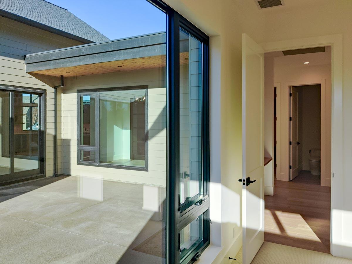 Modern home interior, showcasing a bright hallway with an open doorway to a light-filled outdoor patio space with large windows.