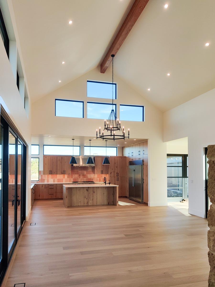 Spacious, modern kitchen with high ceilings, wooden cabinets, and an island. Natural light streams through the large windows, enhancing the open-concept design.