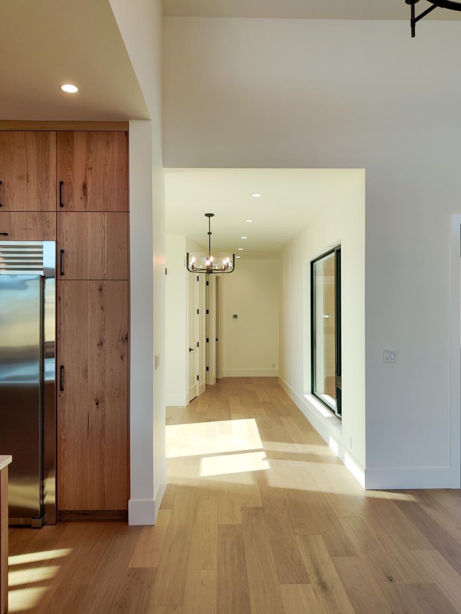 Bright, modern home interior featuring wood floors and cabinetry, leading to a long hallway. A chandelier hangs in the center of the hallway.