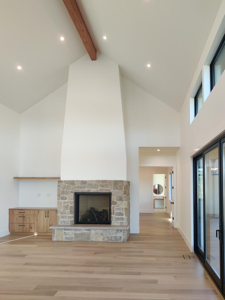 Spacious interior featuring a stone fireplace, light wood flooring, and a high vaulted ceiling with a wooden beam, creating a modern design.
