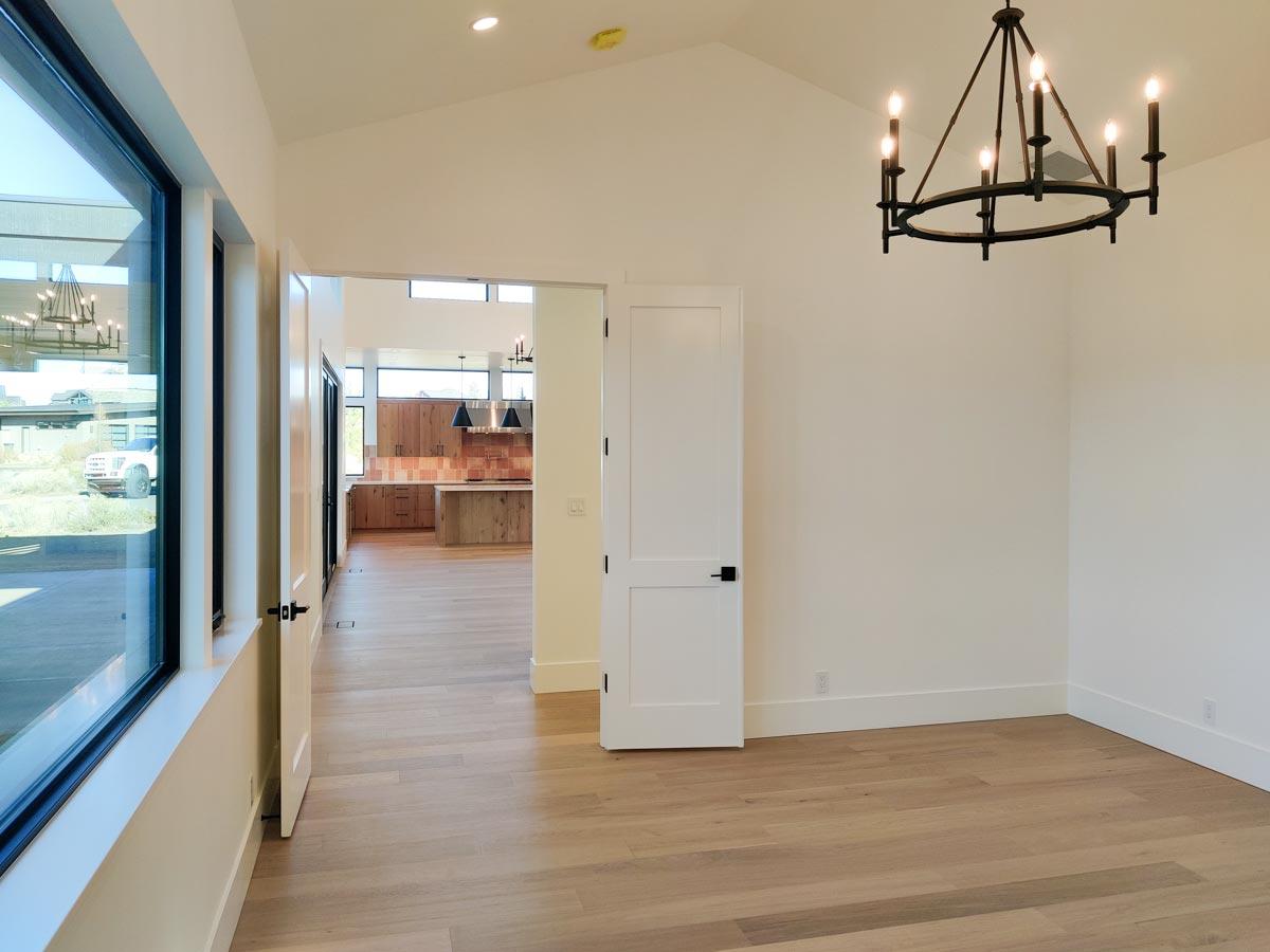 A modern, open-concept home interior with light wood floors, a black chandelier, and a view into the kitchen area.
